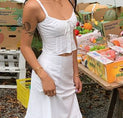 a woman in a white dress standing next to a table filled with fruit