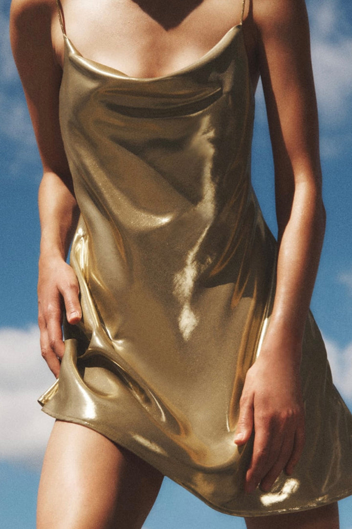a woman in a gold dress standing on a beach