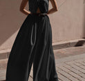 a woman in a black jumpsuit standing on a sidewalk
