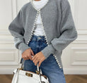 a woman wearing a grey sweater with pearls and a white bag