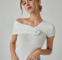a woman wearing a white top with a flower on the shoulder