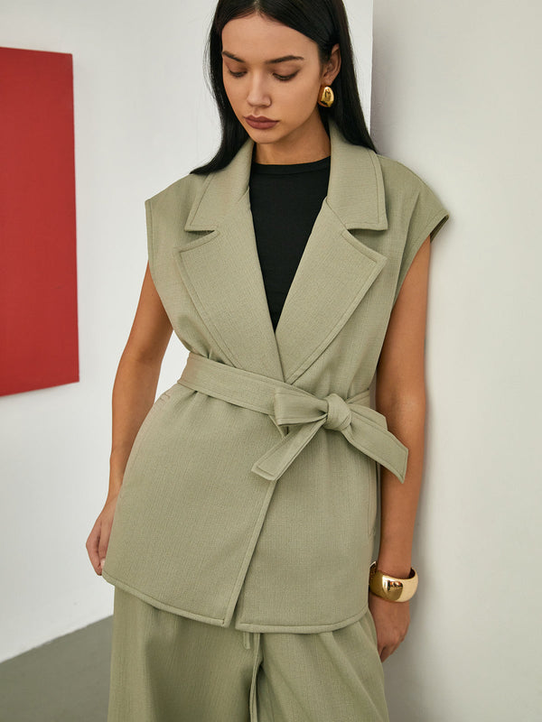 a woman in a green suit leaning against a wall