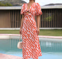 a woman in an orange and white dress standing by a pool
